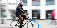 Ein Mann fährt mit einem Swapfiets-Fahrrad an Gebäuden vorbei, im Hintergrund Passanten