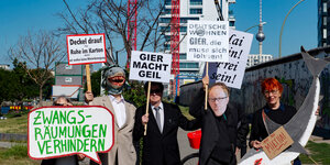 Mitglieder und Anhänger des Bündnisses gegen Verdrängung und Mietenwahnsinn stehen mit Schildern und einer Maske des Deutsche Wohnen Chefs Zahn an der East Side Gallery