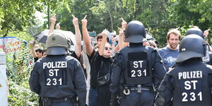 Linke stehen hinetr einer Polizeikette und zeigen Mittelfinger