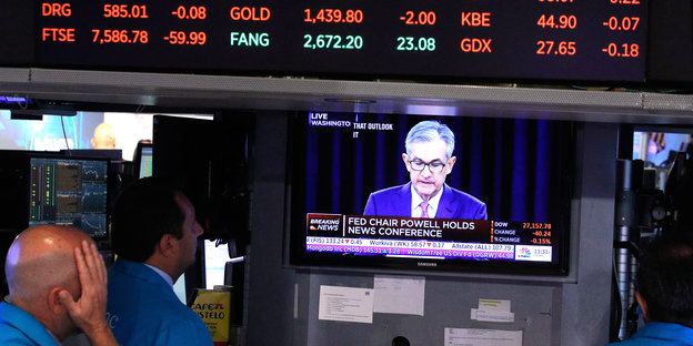 Börsenunternehmer beobachten den Bildschrim, auf dem Jerome Powell die Zinswende ankündigt