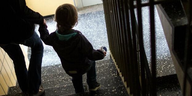 Ein Kind geht an der Hand einer erwachsenen Person die Treppe herunter