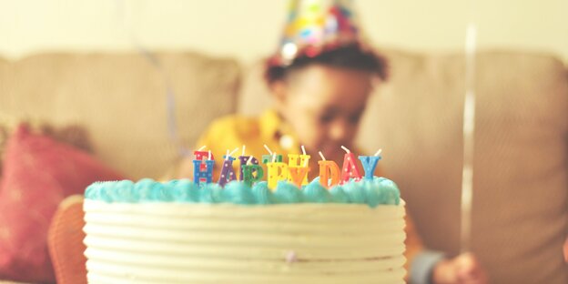 Ein Geburtstagskuchen steht vor einem Kind mit Partyhut
