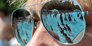 Freibad-Ranking: In einer Sonnenbrille spiegeln sich Freibad-Besucher*innen