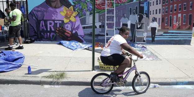 Ein Junge fährt in der Stadt Baltimore mit seinem Fahrrad vor einer bunt bemalten Wand