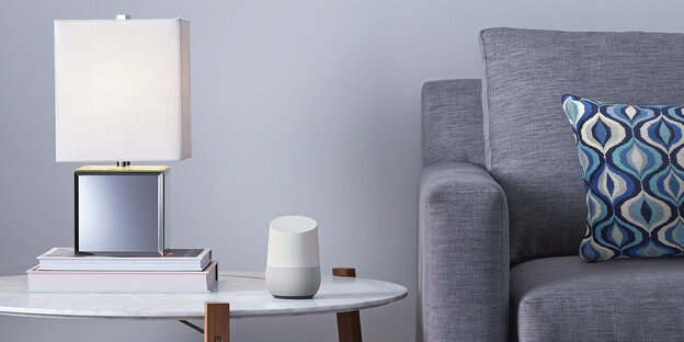 Ein Google Home Lautsprcher steht auf einem Tisch neben einer Couch.