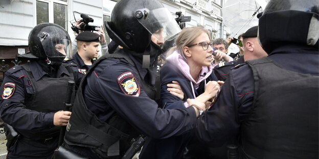 Eine blonde Frau - Oppositionskandidatin in Russland- wird von Polizisten festgenommen