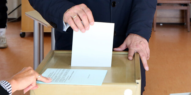 Eine Hand steckt einen WAhlzettel in eine Wahlurne