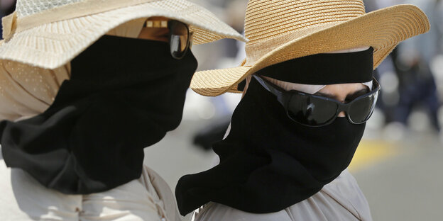 Zwei Musliminnen mit Sonnenhut, Sonnenbrille und schwarzem Mundschutz