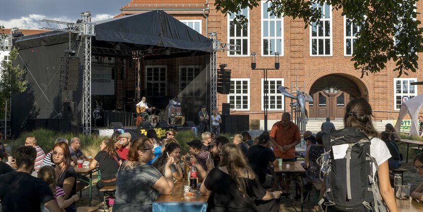 Menschen sitzen auf Bierbänen auf eienr Bühne spielt ein Musiker