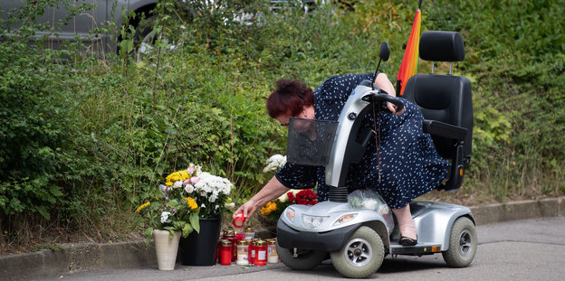 Frau im Rollstuhl legt Blumen ab