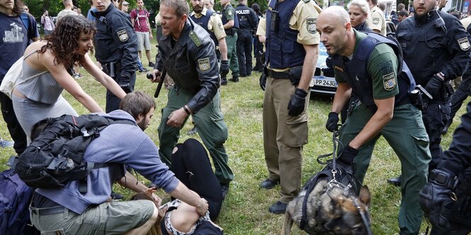 Polizisten greifen Aktivisten mit Knüppeln an und haben einen Hund dabei, eine Aktivistin liegt am Boden