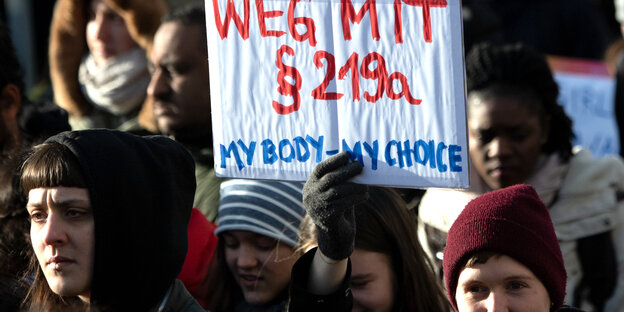Eine Person in einer Menschengruppe auf einer Demonstration hält ein Schild auf dem steht: "Weg mit §219a. My Body - My Choice"