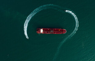 Ein rotes Schiff von oben, umkreist von zwei kleinen Schiffen