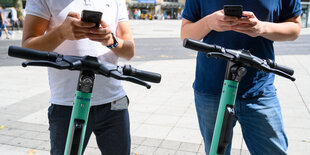 Zwei Lenker von Rollern, dahinter jeweils die Hände von zwei Männern, die auf dem Handy herumtippen