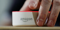 Eine Hand greift nach einerm Lautsprecher von Amazon