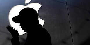 Silhouette eines Menschen der in sein Telefon spricht. Im Hintergrund das Apple-Logo