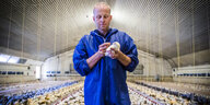 Ein Mann im blauen Overall steht in einem Stall voller Hühner und streichelt ein Küken in seiner Hand