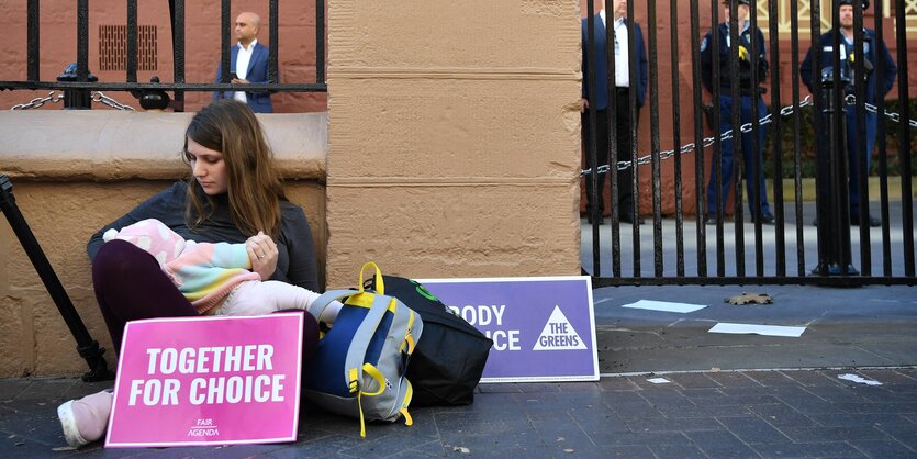 Eine_Frau_und_ihr_Kind_demonstrieren_in_Sydney_fuer_das_Recht_auf_Abtreibung._Die_Frau_sitzt_vor_einem_Gebaeude_in_den_armen_ihr_Baby