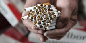 Ein Mitarbeiter der Zollfahndung hält am Freitag (21.07.2011) gefälschte Marlboro-Zigaretten über weiteren Stangen mit gefälschten Zigaretten in einer Lagerhalle in Hamburg.