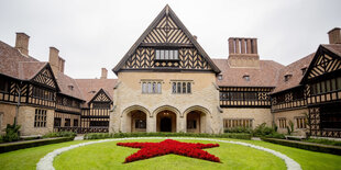 Das Schloss Cecilienhof. Vor dem Mittelbau ist eine Wiese, auf der aus Blumen ein roter Stern wächst.