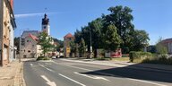 Eine leere Straße in Freital, von Bäumen gesäumt und mit dem Rathaus und einigen Wahlplakaten im Blick