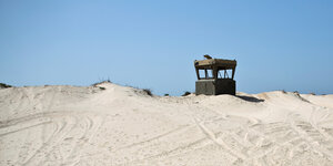 Wachturm, der aus Sandhügeln herausragt - vor blauem Himmel