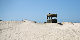 Wachturm, der aus Sandhügeln herausragt - vor blauem Himmel