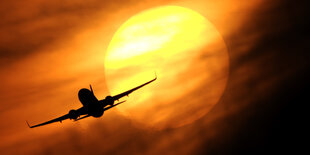 Ein Flugzeug startet am Flughafen in Düsseldorf vor der untergehenden Sonne.