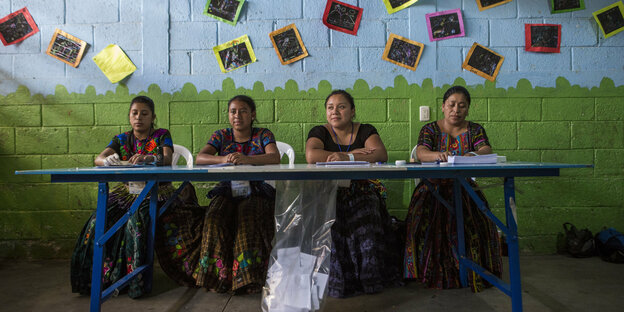 Frauen sitzen hinter einem Tisch. Es ist ein Wahllokal in Guatemala.