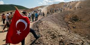 Mehrere Menschen laufen eine sandige Straße hinauf, im Vordergrund trägt jemand eine Türkeiflagge