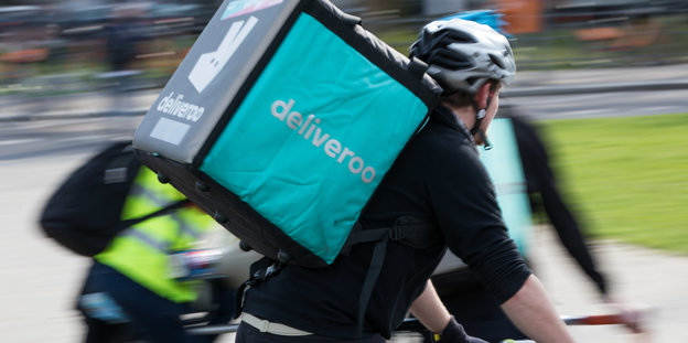 Ein Mann fährt auf einem Fahrrad, er trägt einen Rucksack von Deliveroo