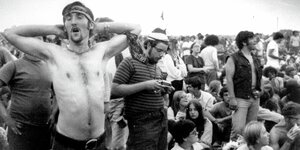 Schwarzweiß-Bild des Woodstock-Festivals, man sieht viele Menschen, im Vordergrund reckt sich ein Mann