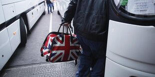 Eine Person steigt in einen Bus mit einer Tasche im Design der britischen Flagge