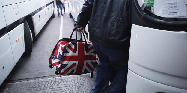 Eine Person steigt in einen Bus mit einer Tasche im Design der britischen Flagge