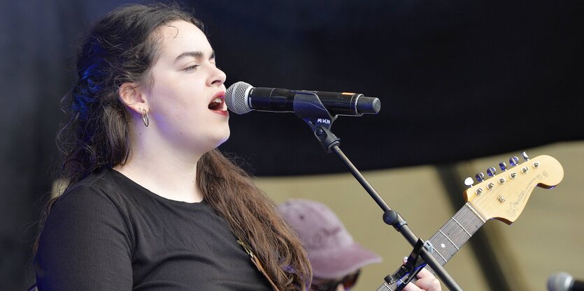 Die Sängerin Ilgen-Nur steht mit ihrer Gitarre am Mikrofon und singt, sie hat langes braunes Haar