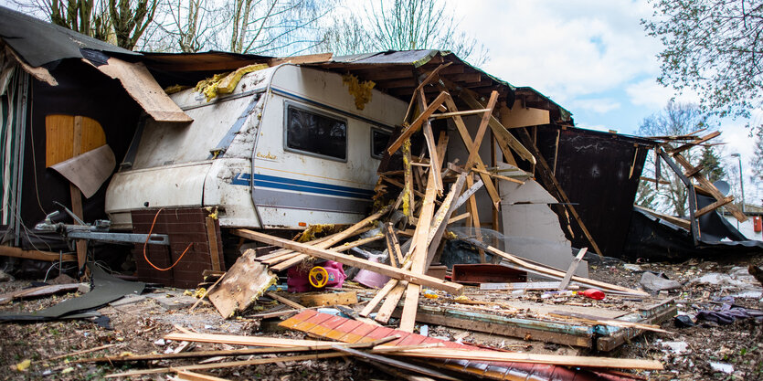 Trümmer und Müll, Bretter und Latten sind um einen alten Campinganhänger zu sehen