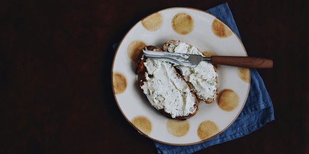 Ein Teller auf dem sich zwei Scheiben Brot befinden, die mit Frischkäse bestrichen sind.