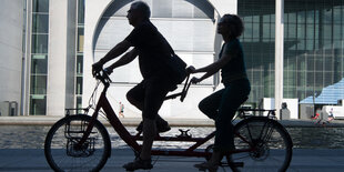 Zwei Menschen fahren auf einem Tandem durch das Regierungsviertel, Aufnahme im Gegenlicht