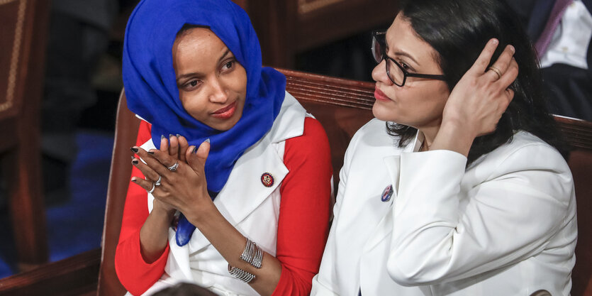 Ilhan Omar und Rashida Tlaib sitzend. Omar klatscht in die Hände.