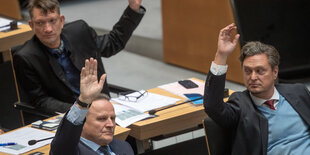 Drei Männer heben den Arm bei einer Abstimmung im Abgeordnetenhaus