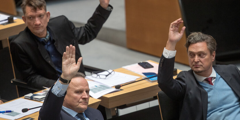 Drei Männer heben den Arm bei einer Abstimmung im Abgeordnetenhaus