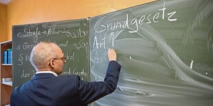 Ein Mann schreibt das Wort "Grundgesetz" auf eine Schultafel.