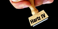 Eine Hand hält einen Stempel mit der Aufschrift "Hartz IV".