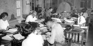 Auf einem schwarz-weiß-Foto sitzen Menschen an Schreibtischen tippen, telefonieren und schreiben