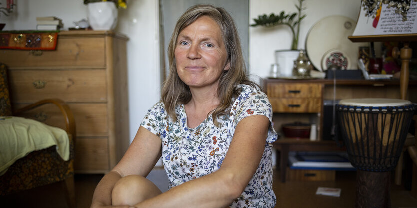 Eine Frau mit grauen langen Haaren sitzt auf dem Boden und lächelt