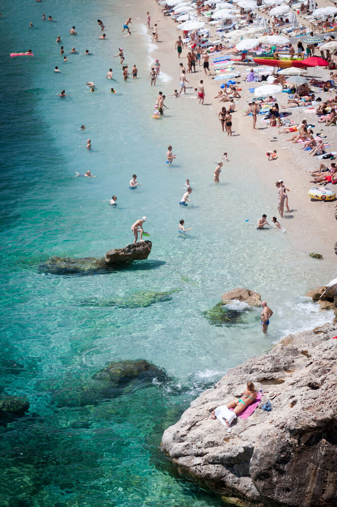 Touristen baden im Meer, im Hintergrund ein voller Strand