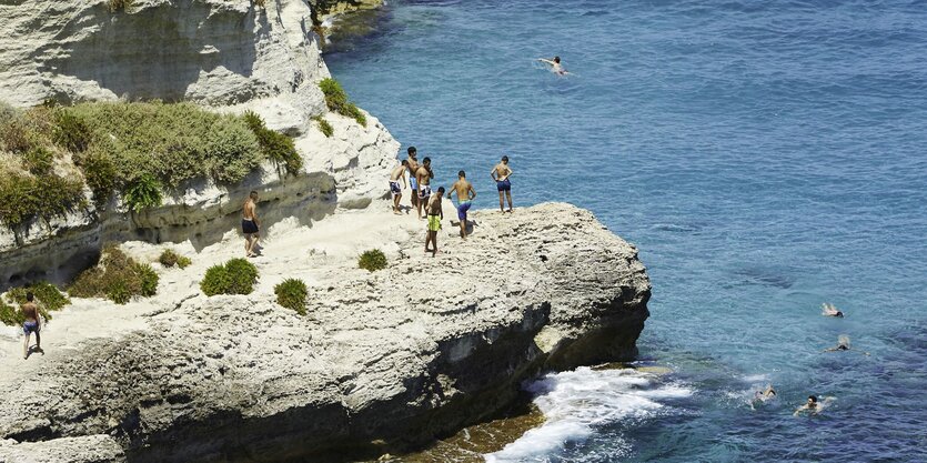 An einer Klippe am Meer schwimmen Menschen im Wasser