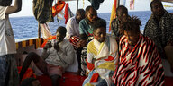 Mehrere Menschen sitzen in Decken gehült an Deck eines Schiffes
