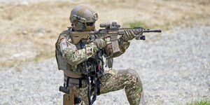 Ein schwer bewaffneter und vermummter Soldat zielt mit seinem Gewehr