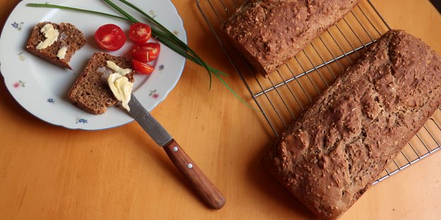 Auf einem Holztisch stehen Brot, Teller Messer und Butter